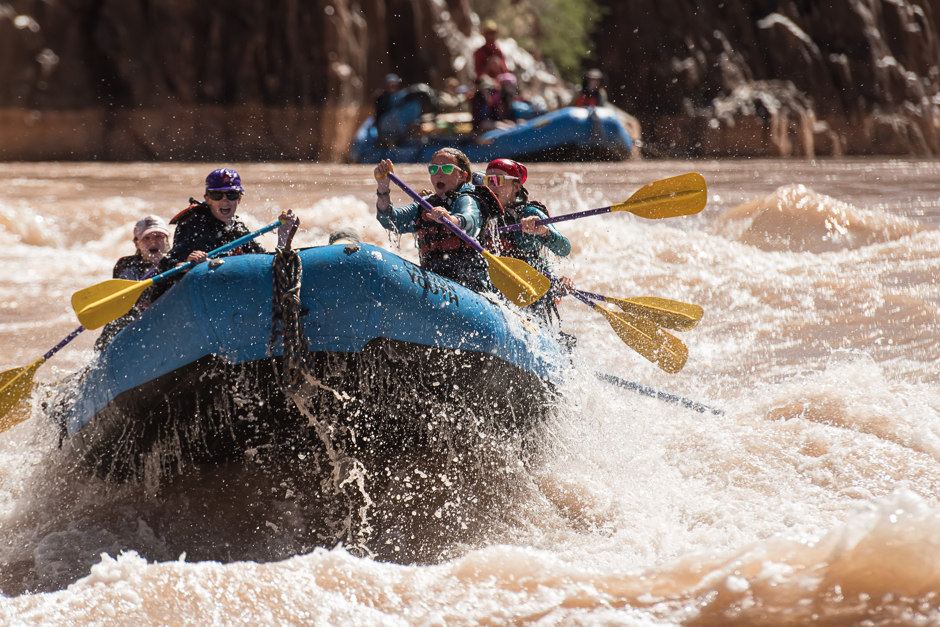 kids hold their paddles up on a raft while splashing through waves